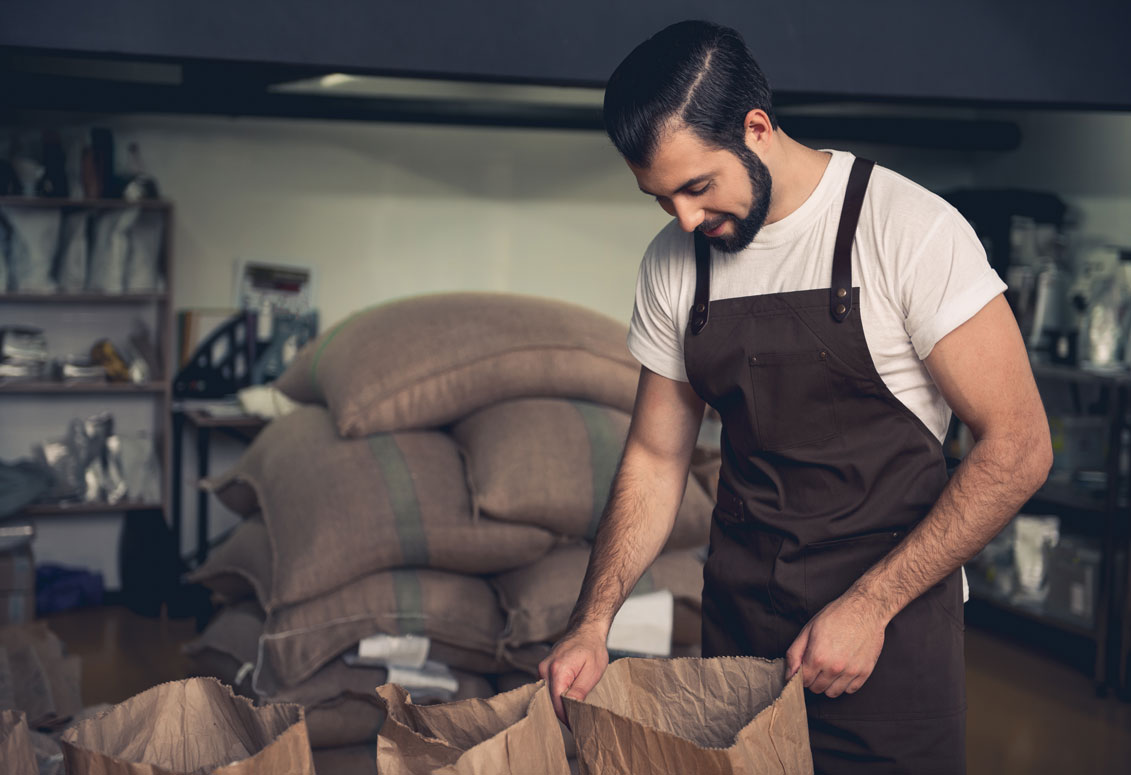 Man wearing apron looking into paper bag of coffee beans