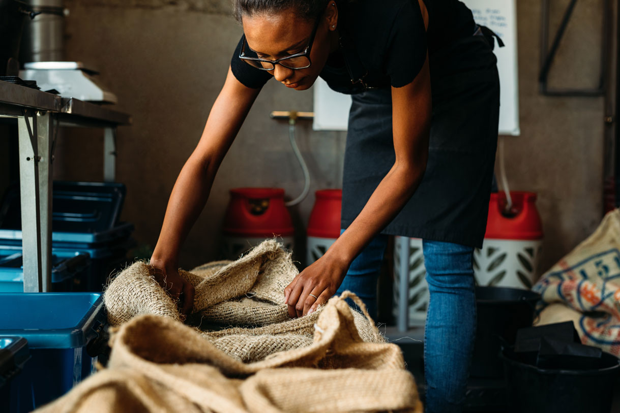 Woman leaning over canvas bag of coffee beans